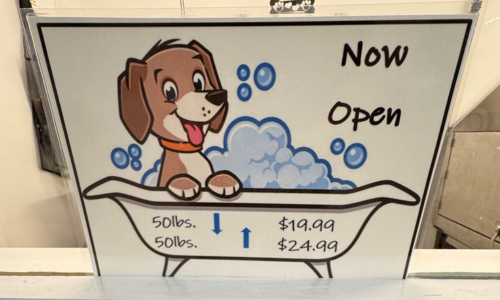 A sign stating that our Self Wash is, 'Now Open!' with a dog in a bathtub which also lists pricing for dogs above and below 50lbs (less than 50lbs $19.99 and more than 50lbs $24.99)